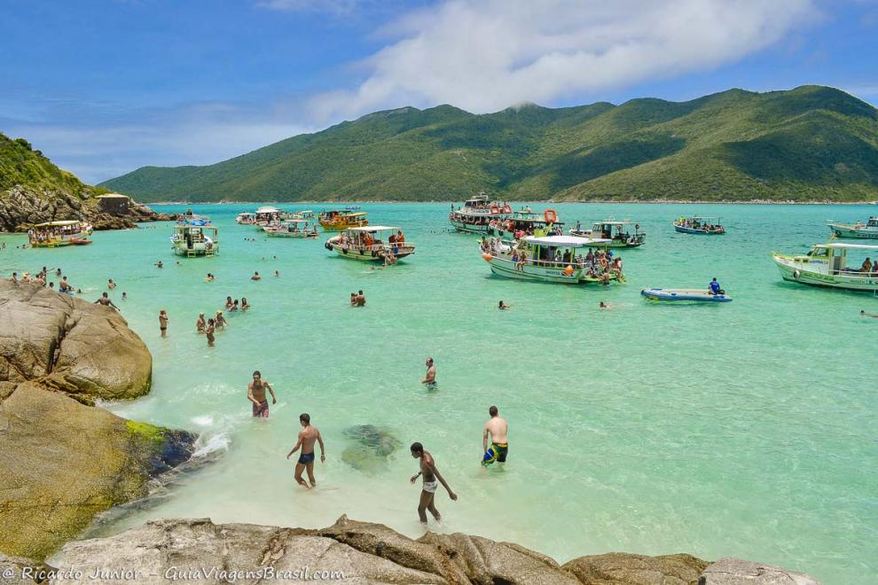 Imagem de vários barcos de passeio e turistas na Praia do Pontal do Atalaia.